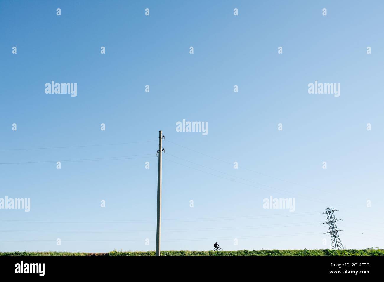 Longshot of a man riding bike along powerlines. Over blue sky. Stock Photo