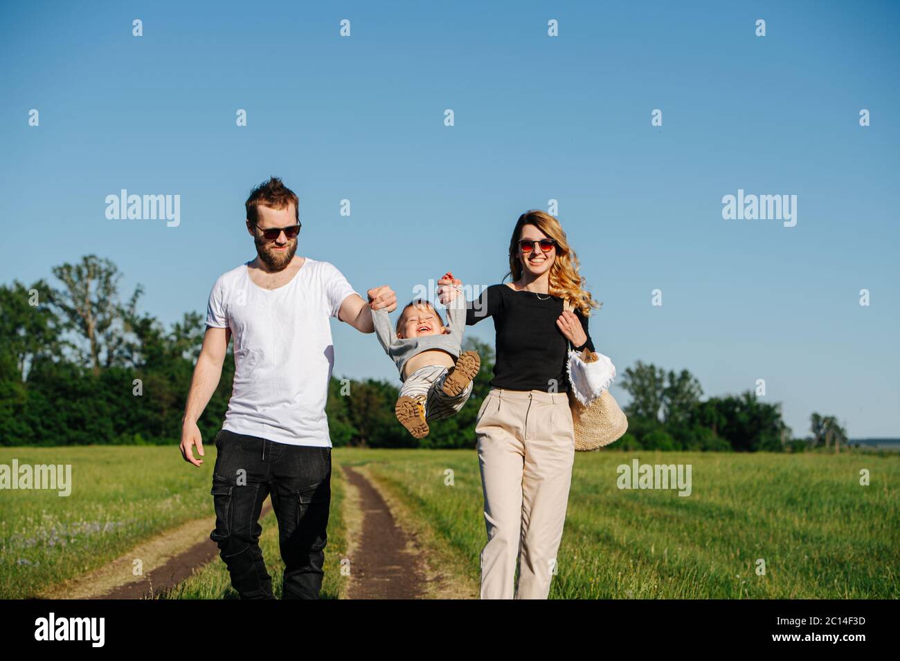 Happy family walking on track, holding baby's hands, swinging him back and forth Stock Photo