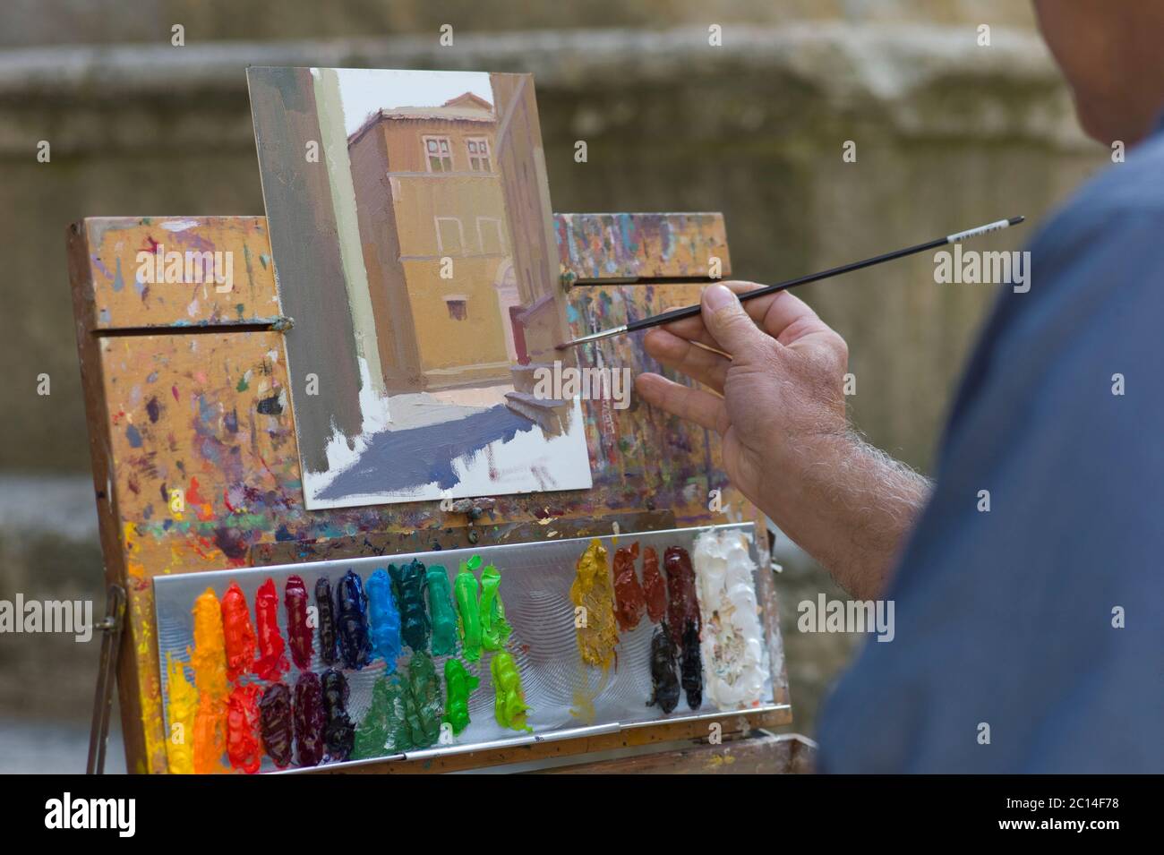 Artist paints a house with acrylic paint and a thin brush on panel in a street in Lucca, Italy on a sunny day Stock Photo