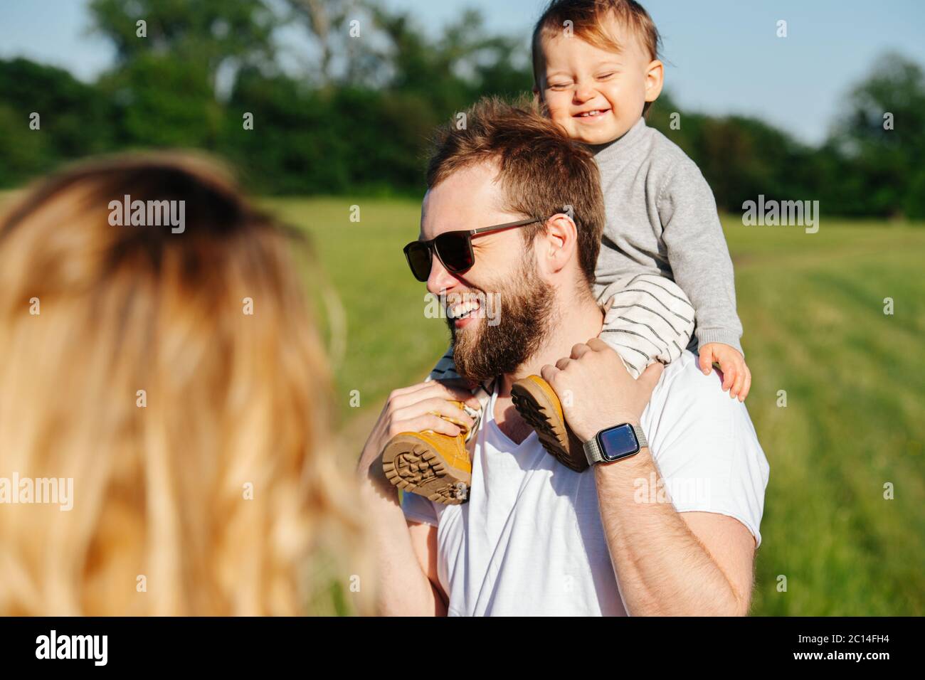 Happy family. Woman watching how her baby riding on dad's shoulders ...