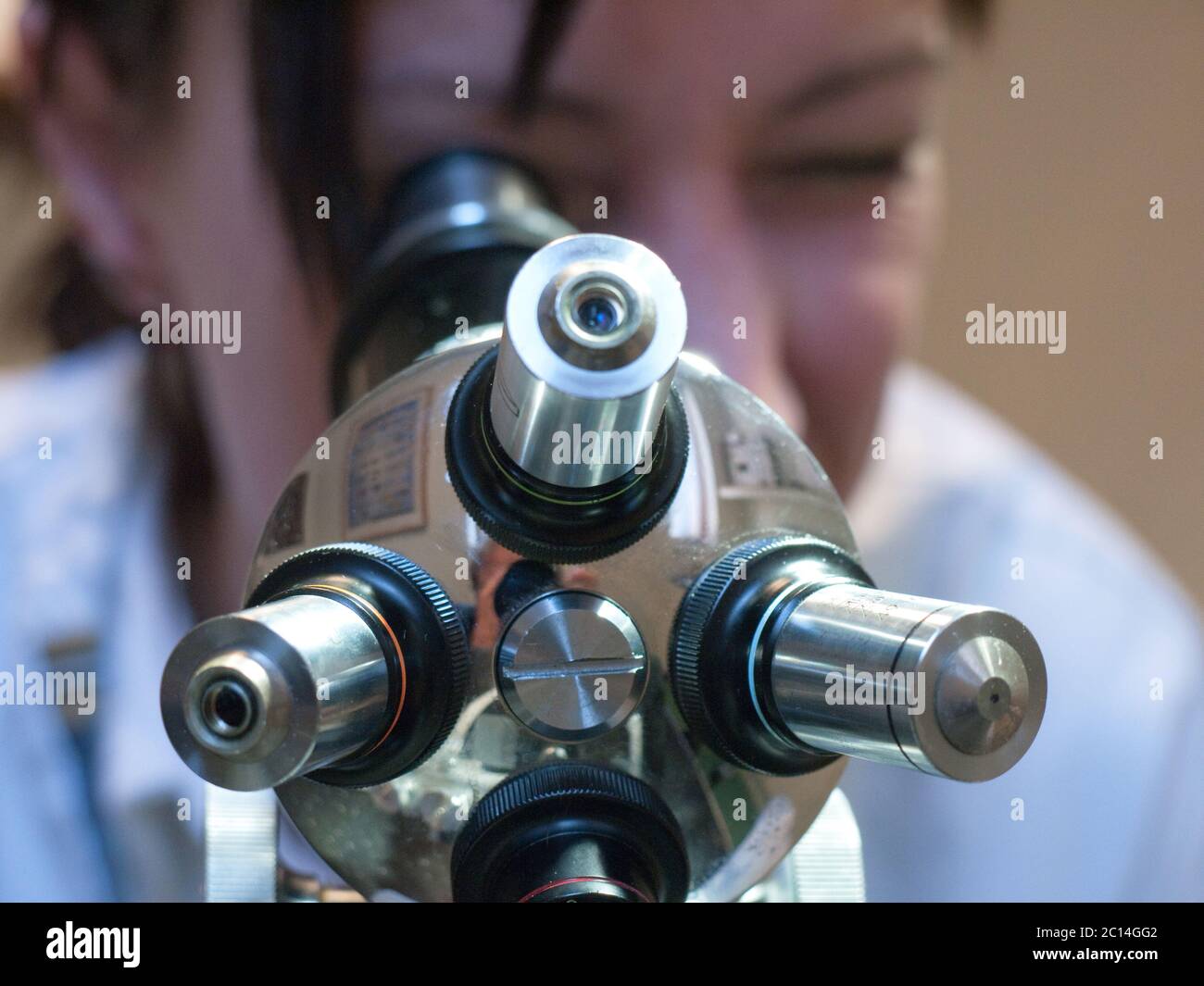 Young woman looks through a microscope. Photo taken from below with focus on the four lenses Stock Photo