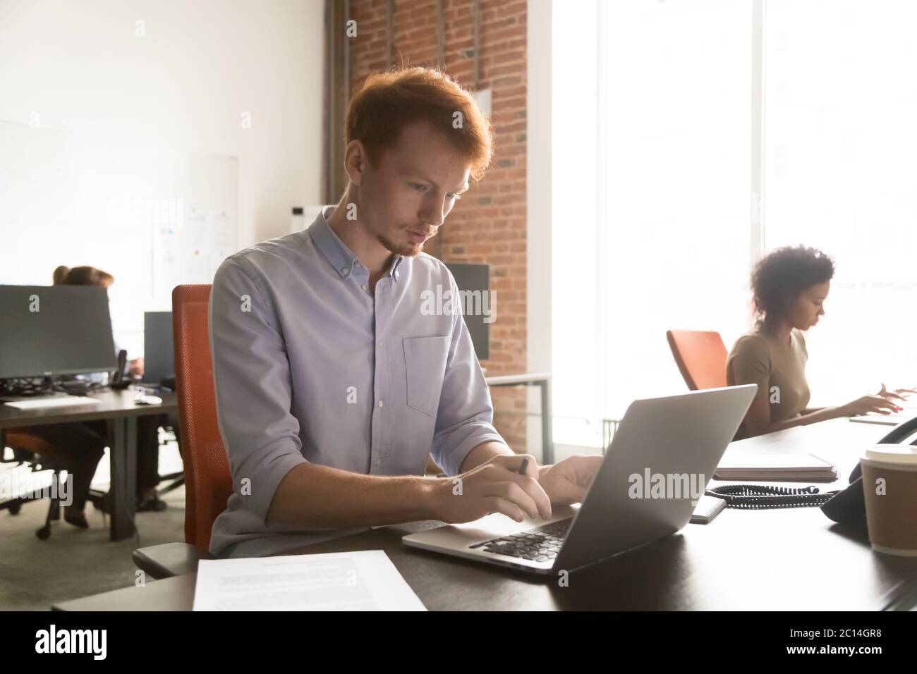 Busy young employee intern using laptop, working with documents Stock Photo
