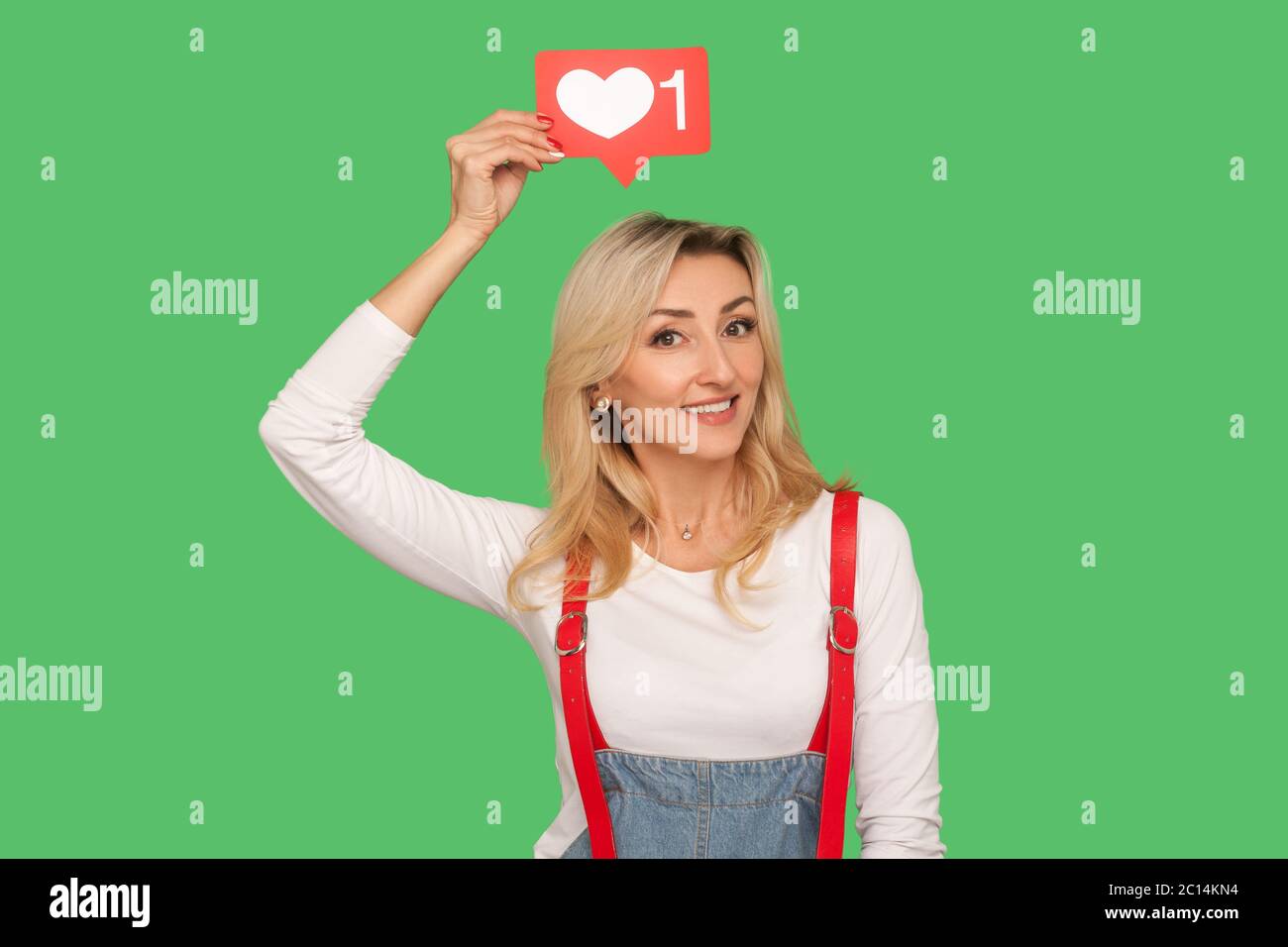 Follow and like social media blog. Portrait of lovely smiling adult woman  in stylish denim overalls holding network heart icon over head, emoji  notifi Stock Photo - Alamy