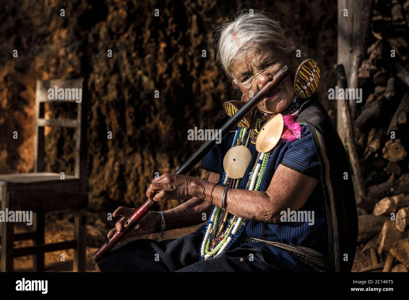 Yaw Shen, a mature K'cho Chin woman with face tattoos, plays traditional nose flute, Chin State, Myanmar Stock Photo