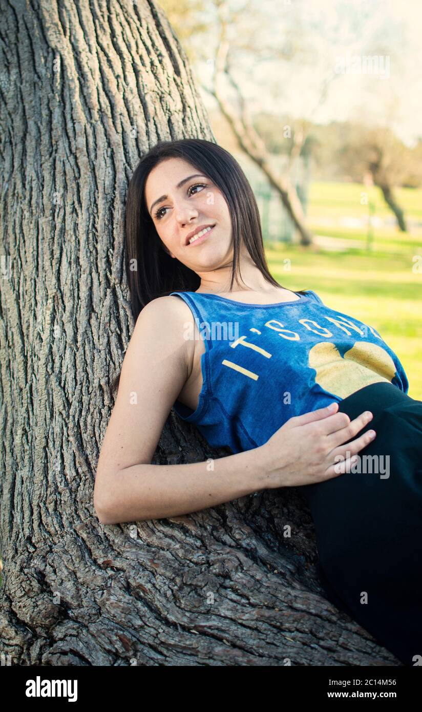 Young middle eastern woman relaxes on a tree trunk in a park Stock Photo