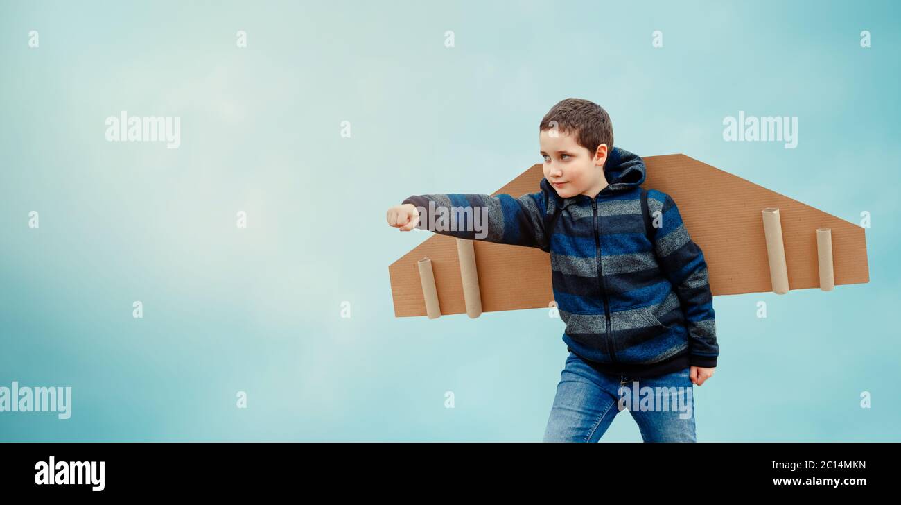 Happy child playing with toy paper wings airplane against the blue sky ...