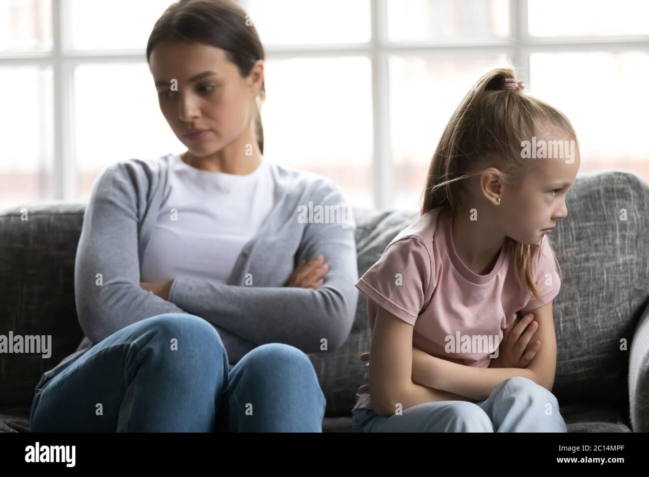 Offended little daughter and mother ignoring each other after quarrel Stock Photo