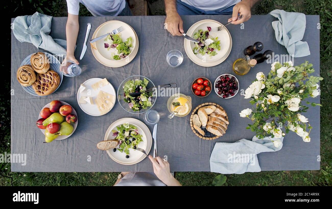 Family dinner outdoors. Family dinner with organic salad and cheese on trendy scandinavian style table in garden. Healthy aesthetic beautiful food, summer staycation concept. Aerial view or top view Stock Photo