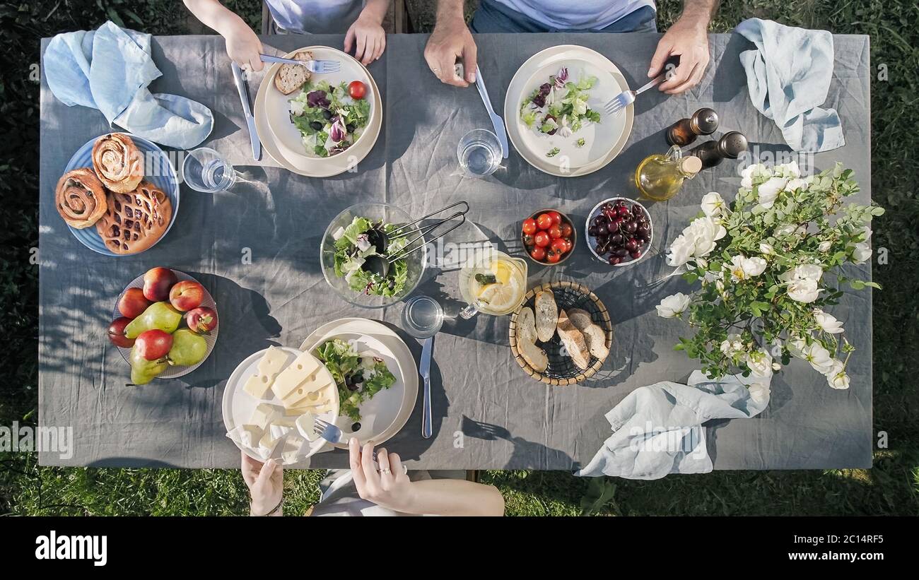 Family dinner outdoors. Family dinner with organic salad and cheese on trendy scandinavian style table in garden. Healthy aesthetic beautiful food, summer staycation concept. Aerial view or top view Stock Photo