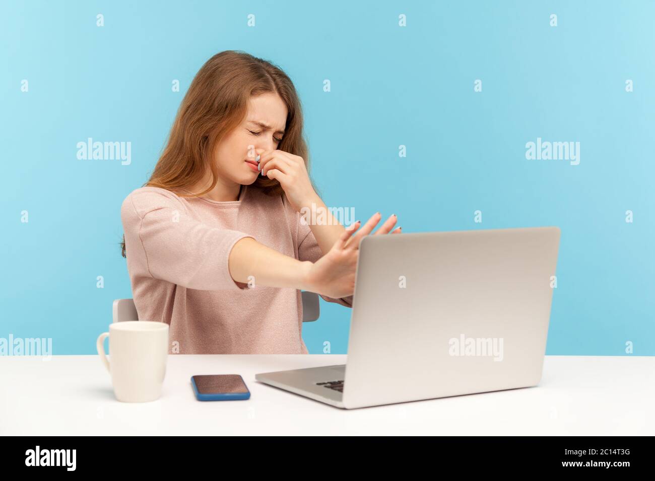 Bad smell. Displeased woman employee holding breath, pinching her nose and gesturing stop at laptop screen, metaphor of stinky shameful internet conte Stock Photo