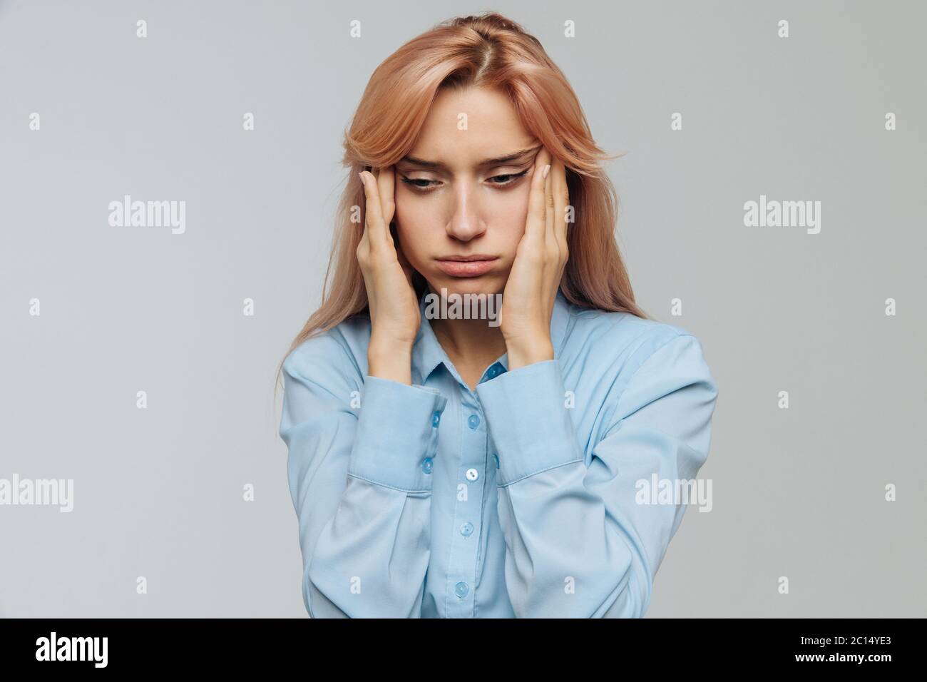 Tired young woman in blue shirt wants to sleep at work or university, opening her eyes with the fingers, squinting so as not to fall asleep. Lack of s Stock Photo