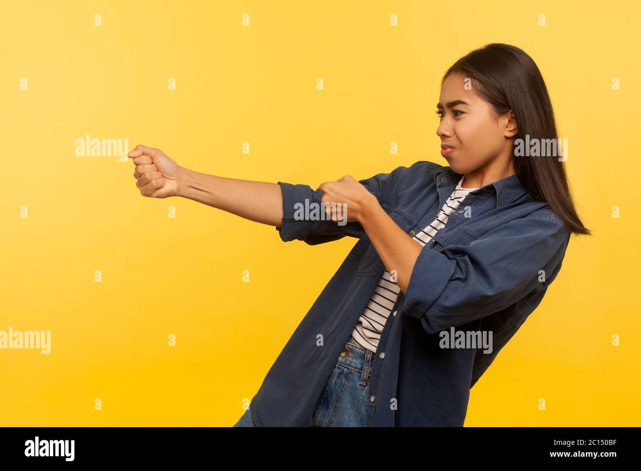 Portrait of diligent purposeful girl in denim shirt pulling invisible heavy burden, striving hard to achieve success, dragging with persistence. indoo Stock Photo