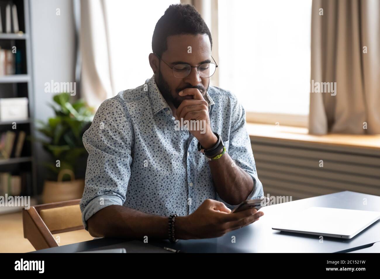 African guy holding smartphone feels concerned thinking over received message Stock Photo