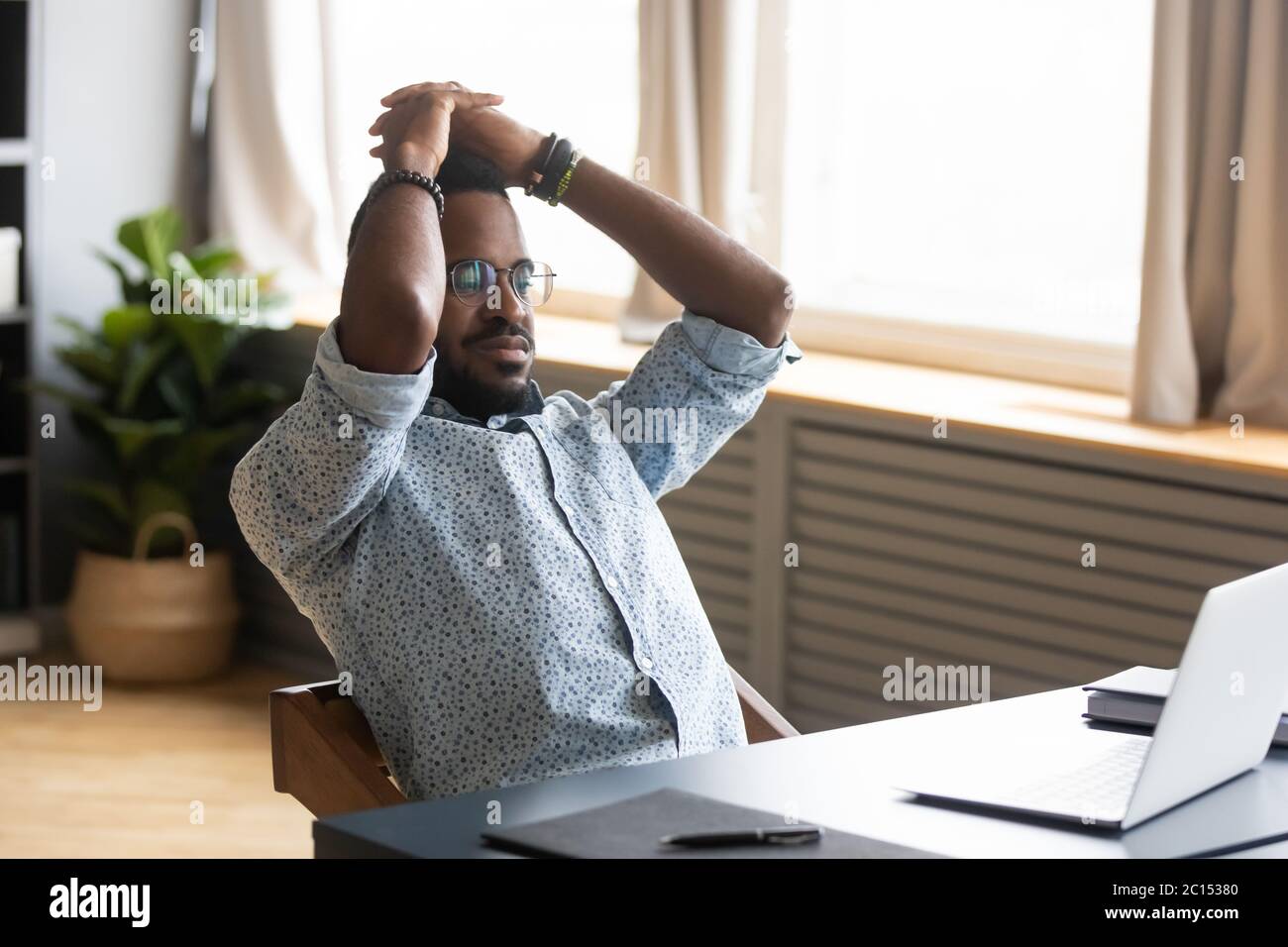African man leaned on office chair resting looking at pc Stock Photo