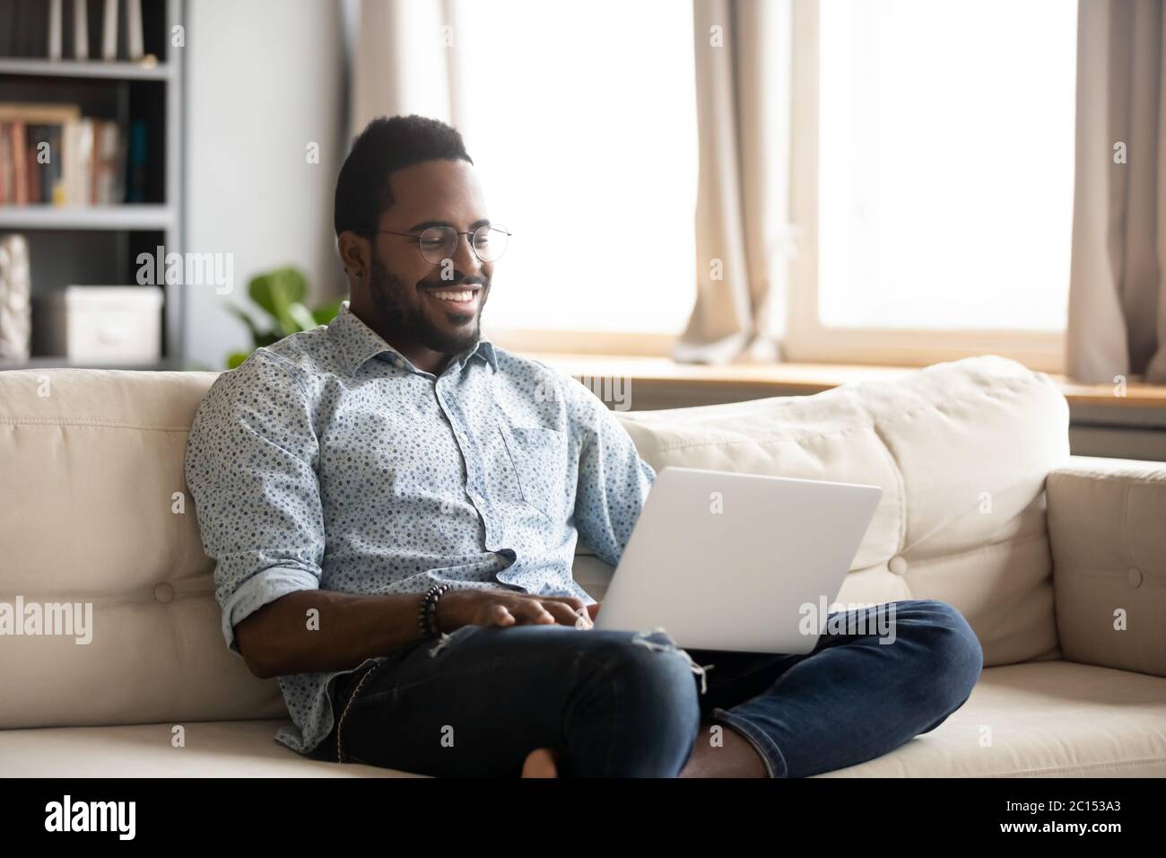 African man sitting on couch smile looking movie using laptop Stock Photo
