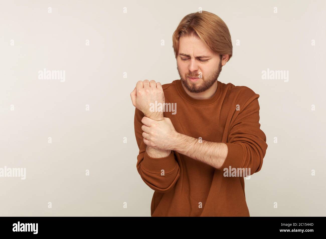 Sprain wrist. Portrait of bearded man in sweatshirt massaging sore arm