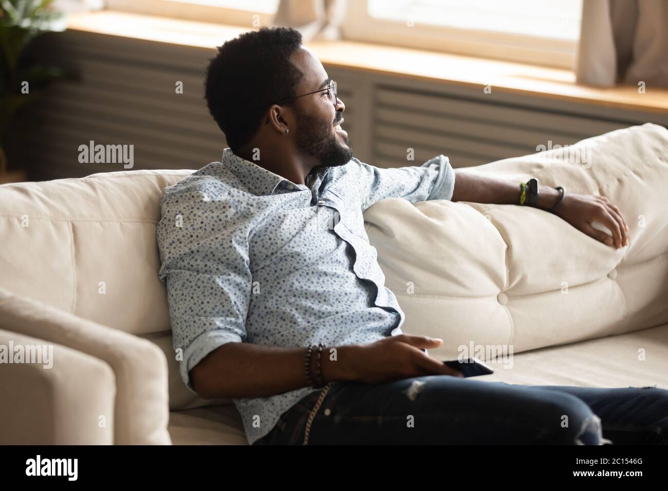 Guy seated on couch breath fresh air looking at window Stock Photo