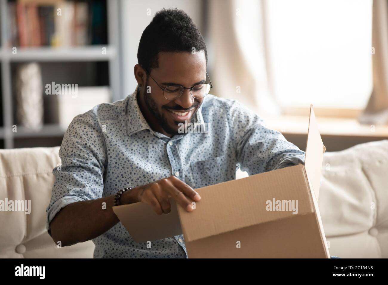 African man opening parcel seated on couch at home Stock Photo