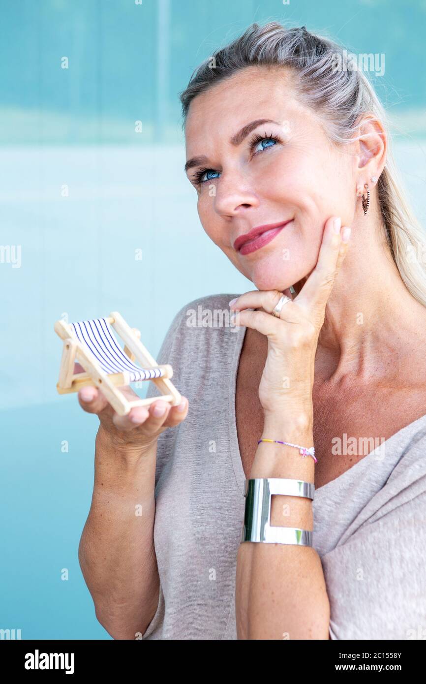 portrait of blond woman holding miniature sun chair and looking longingly Stock Photo