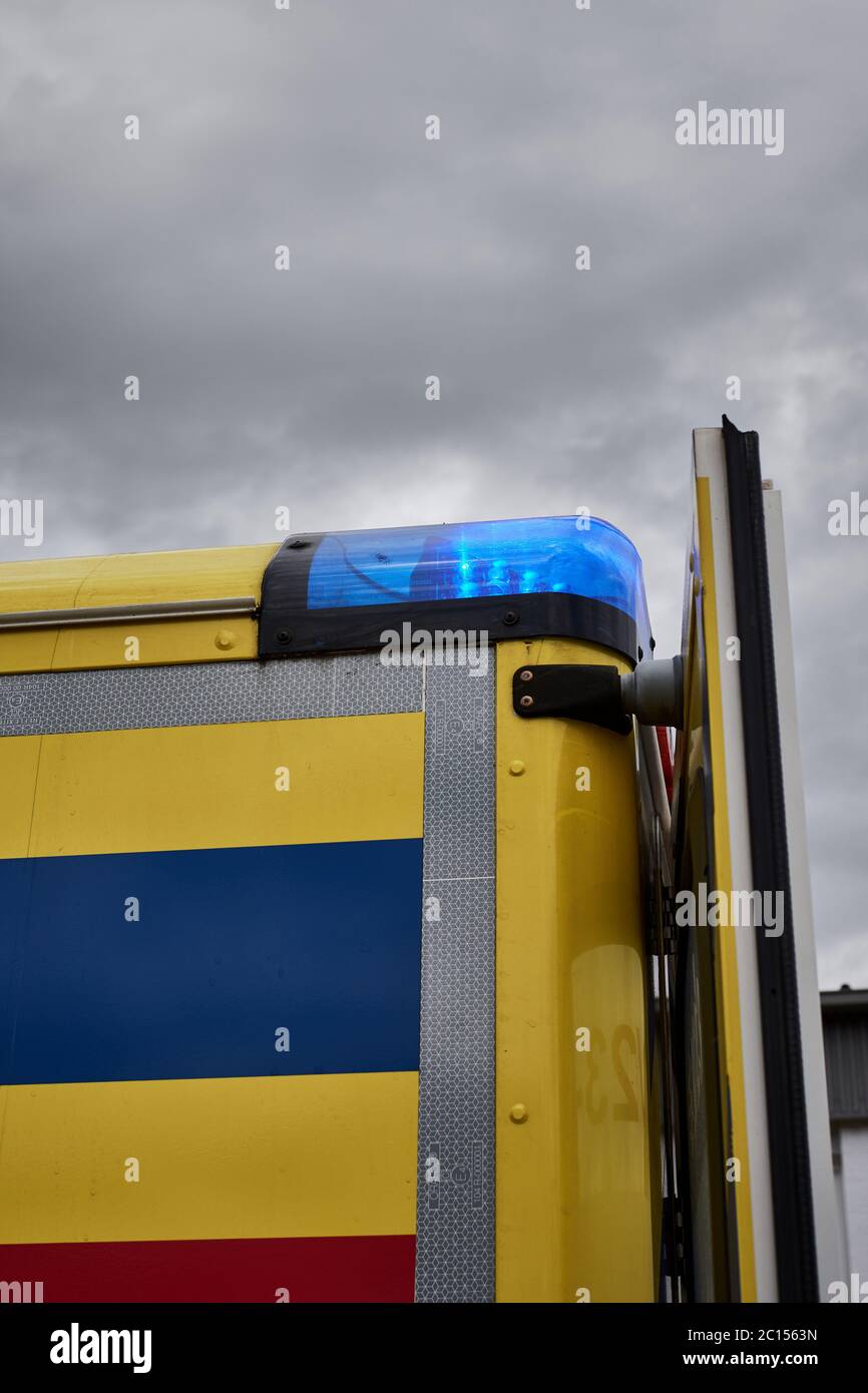 Ambulance vehicle with emergency blue light on against overcast sky Stock Photo