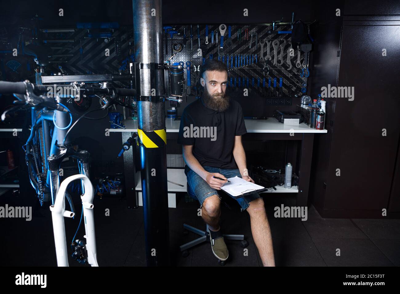 Stylish bicycle mechanic making notes in clipboard in workshop. theme ...