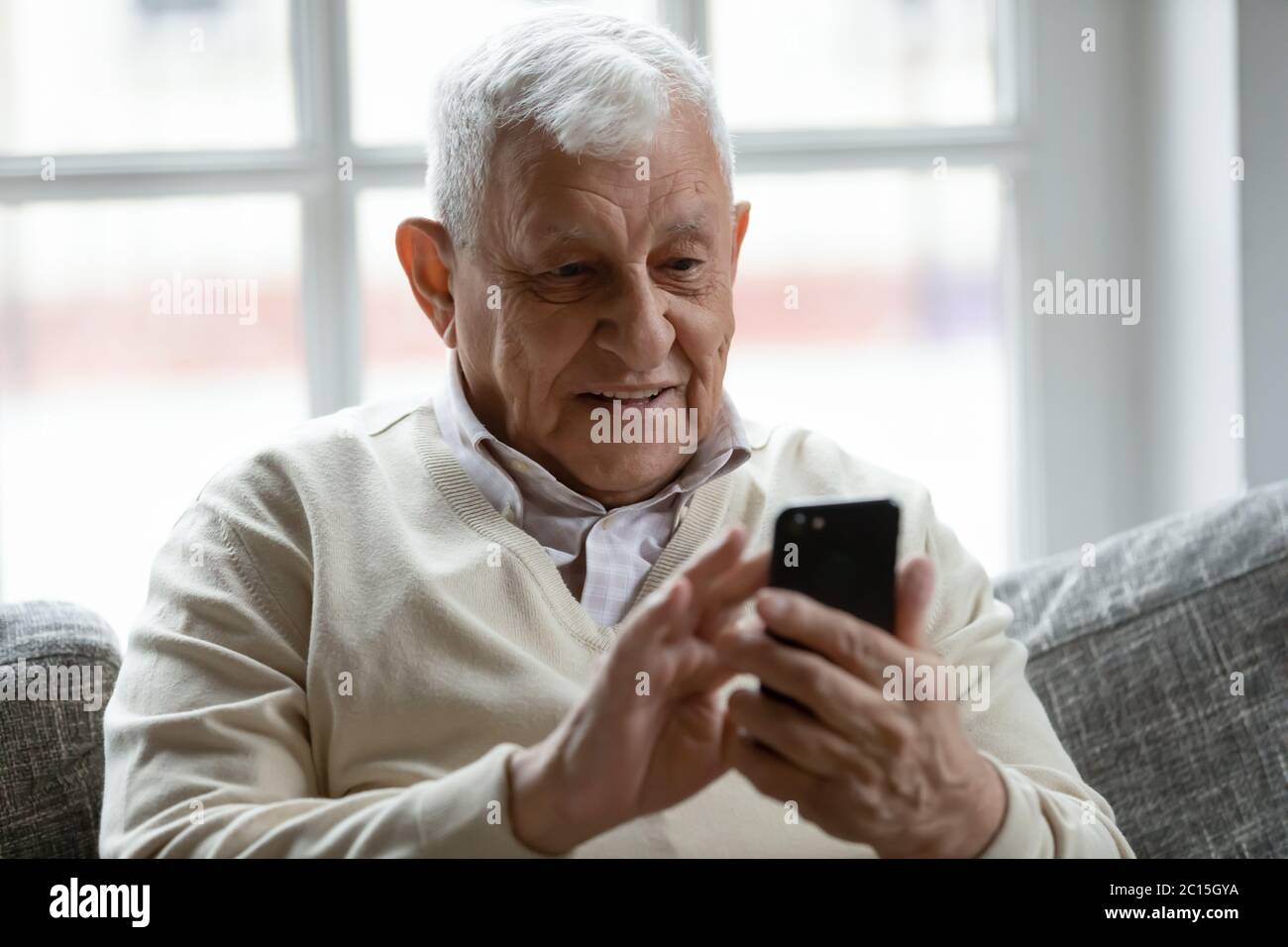 Close up smiling older man using phone, looking at screen Stock Photo