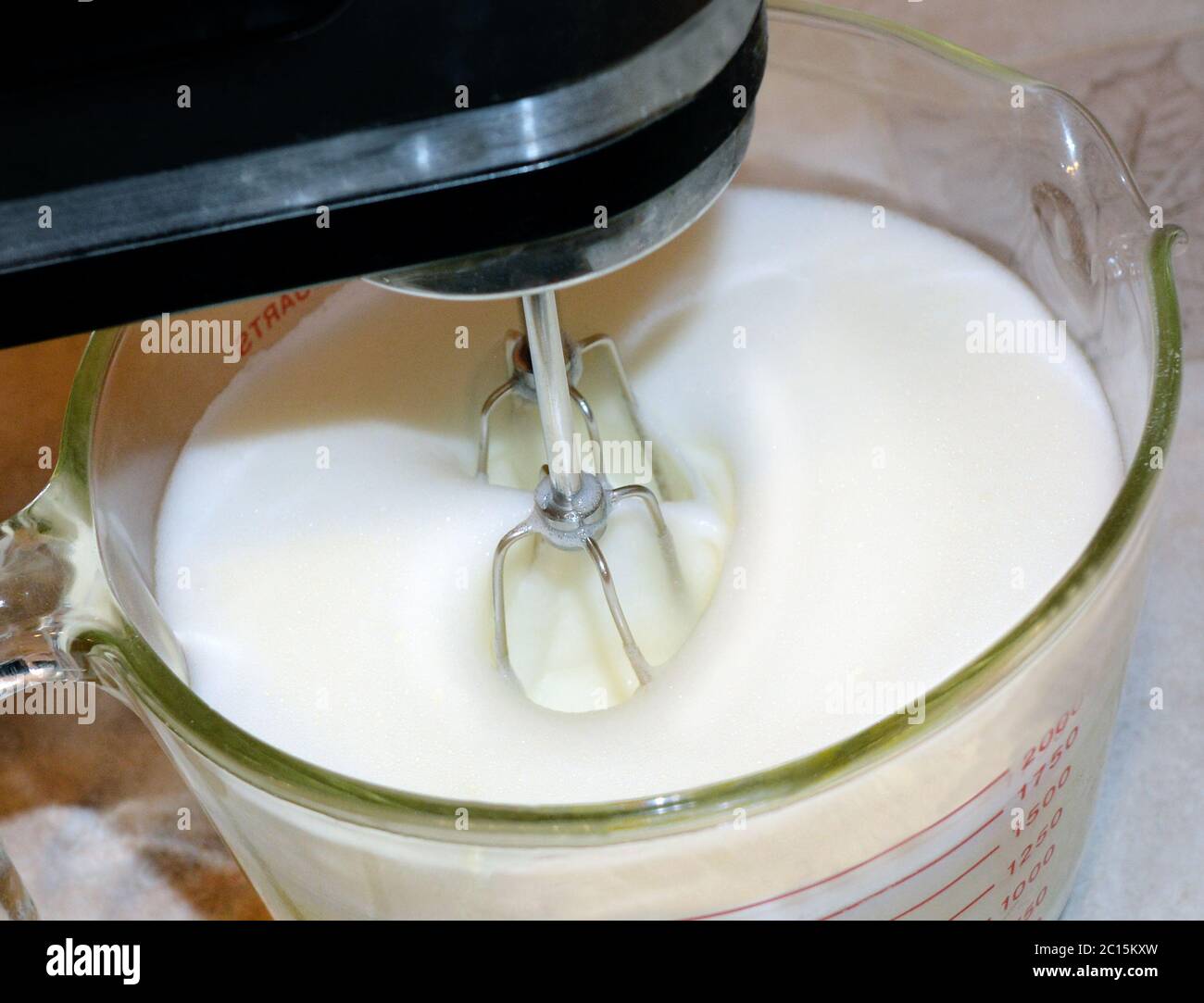 Close up photo of a mixer whipping ingredients in a glass bowl. Stock Photo