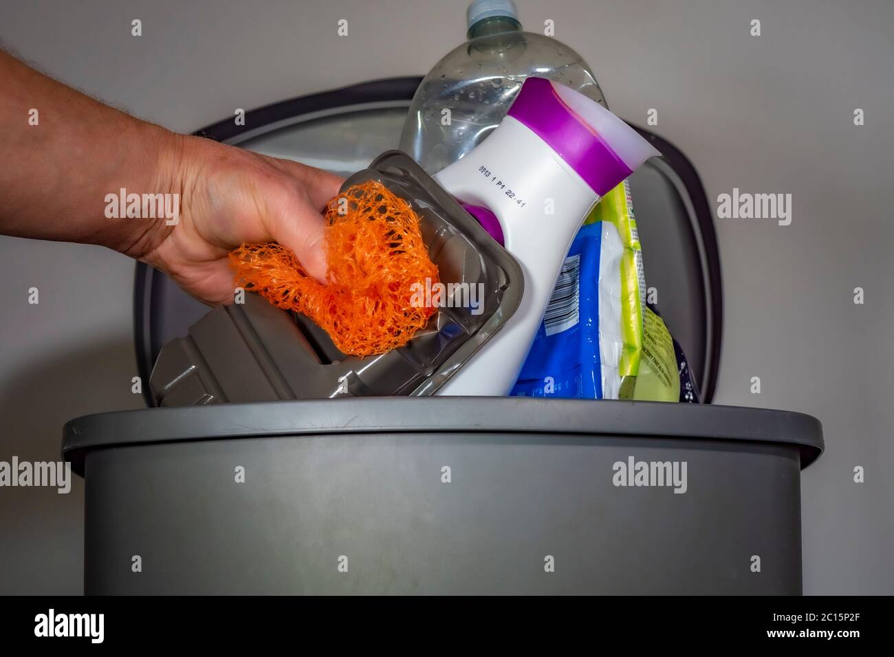 A man’s hand placing mixed plastic household waste / trash items into a