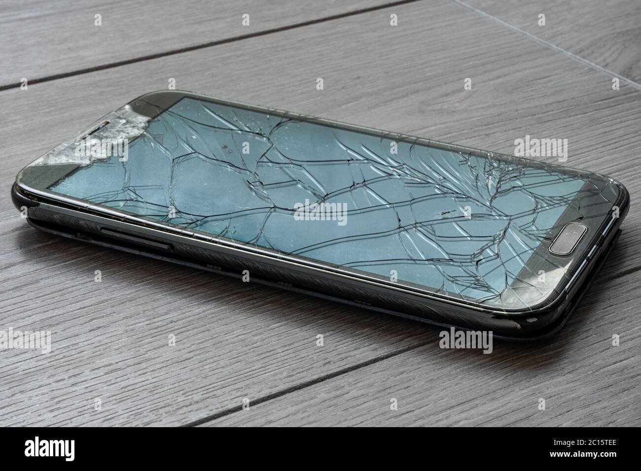 Broken smartphone on the floor. The screen is cracked and the phone is damaged. Stock Photo
