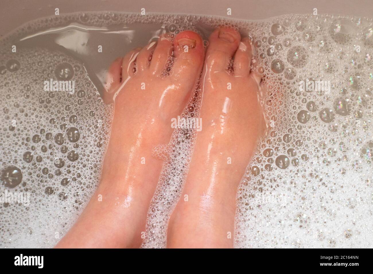 Washing little child feet in bubbling and foamy water. Close-up. Stock Photo