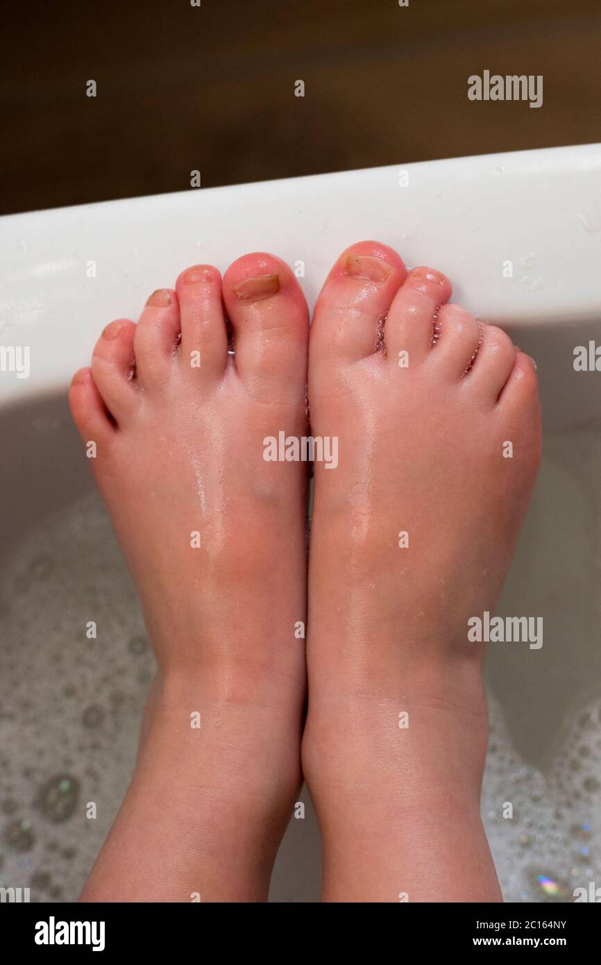 Washing little child feet in bubbling and foamy water. Close-up. Vertical shot. Stock Photo