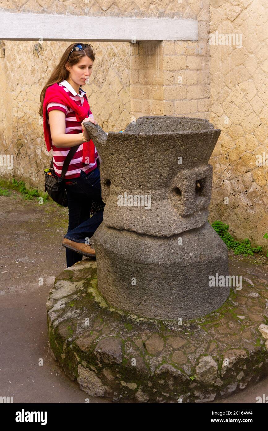 A female woman tourist looking into the millstone within the bakery (pistrinum e Bottega di) of Sextus Patulcius Felix, Herculaneum, Italy Stock Photo