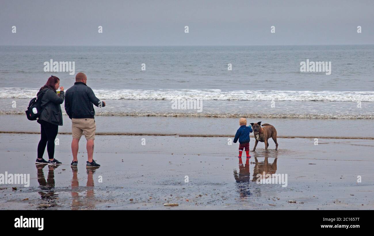 Portobello, Scotland, UK. 14 June 2020. After yesterday's fog all day, it turned a little brighter  and warmer today but still dreich with cloudy skies, temperature of 16 degrees centigrade. Busy seaside with all the cafes and pub open, pictured: three female paddle boarders and one family at the seashore. Stock Photo