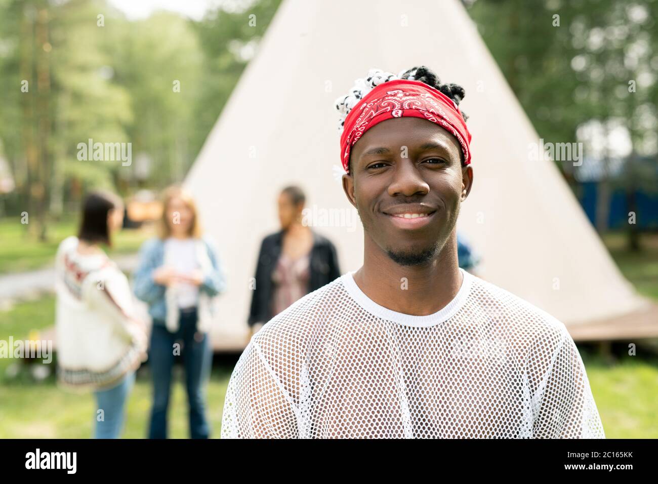Portrait of smiling handsome young black man with beard wearing red bandana spending time at festival campsite Stock Photo