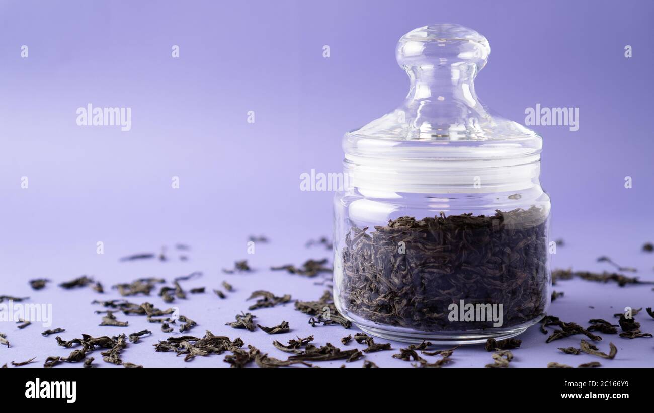 Large leaf black tea in glass jar. Leaf tea. Leaves of green tea in bottle. Purple background. Place for message. High quality photo Stock Photo