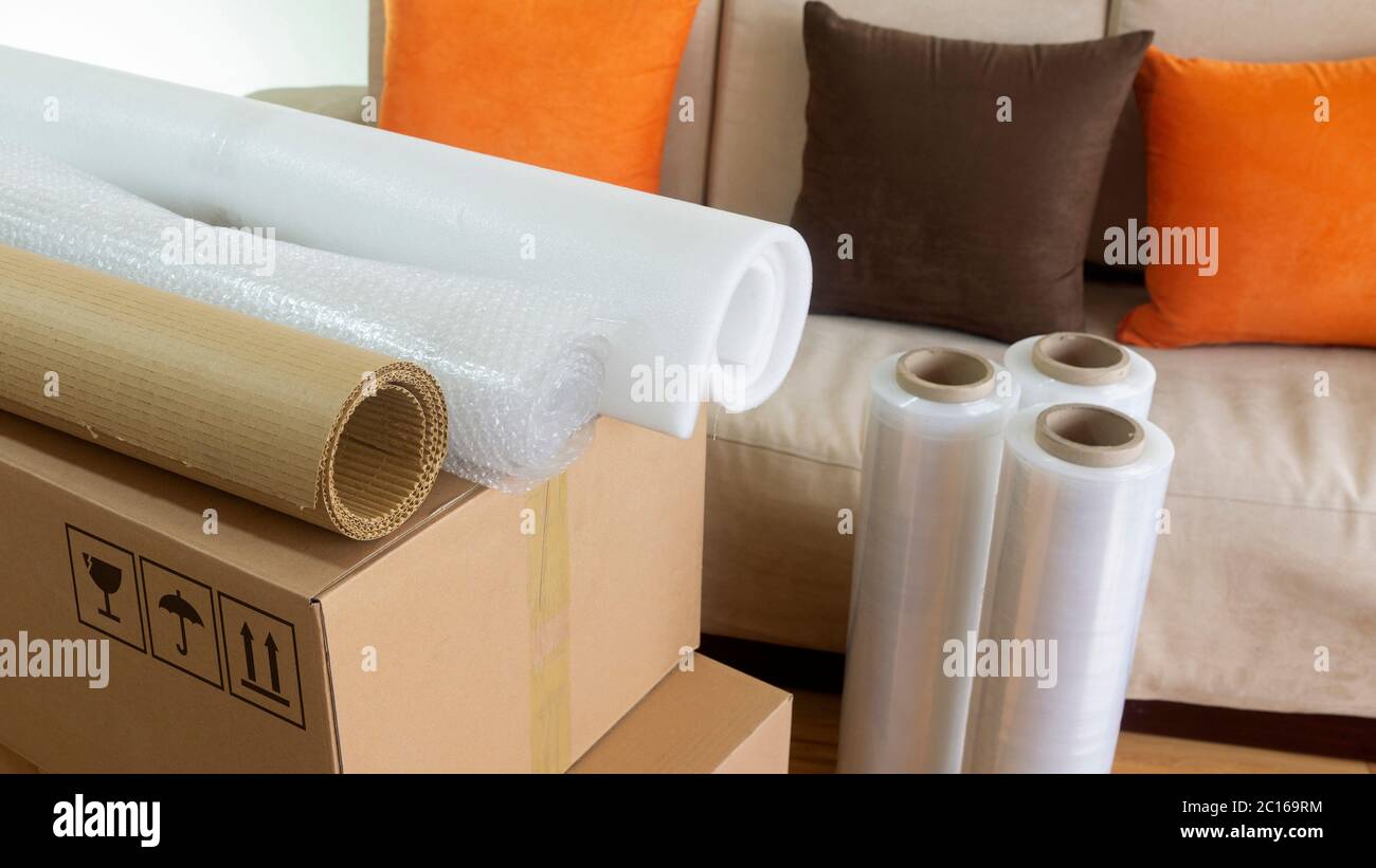 Approach to three rolls of cardboard, foam and bubble wrap used to pack things on a cardboard box with a sofa in the background Stock Photo