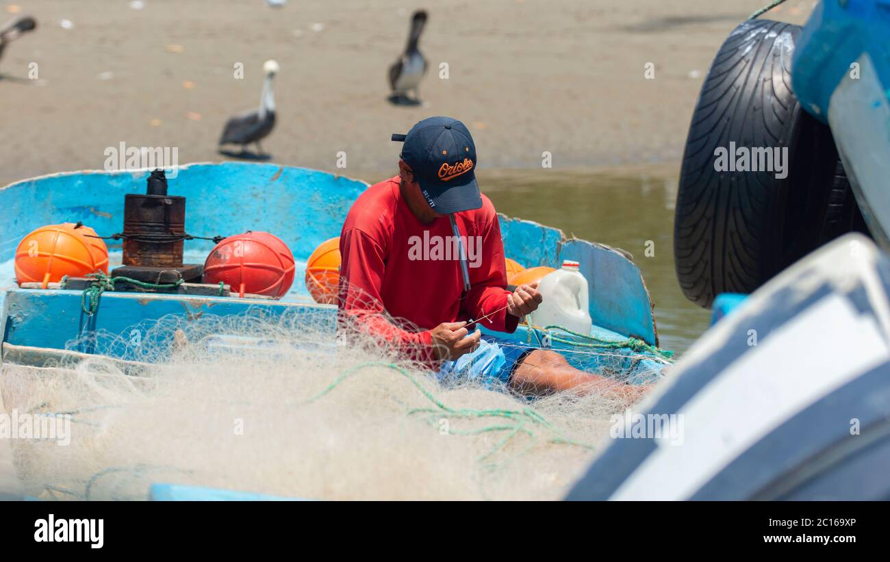 Palmar, Santa Elena / Ecuador - October 19 2019: Artisanal fisherman sewing his net on his boat by the river with birds in the background Stock Photo