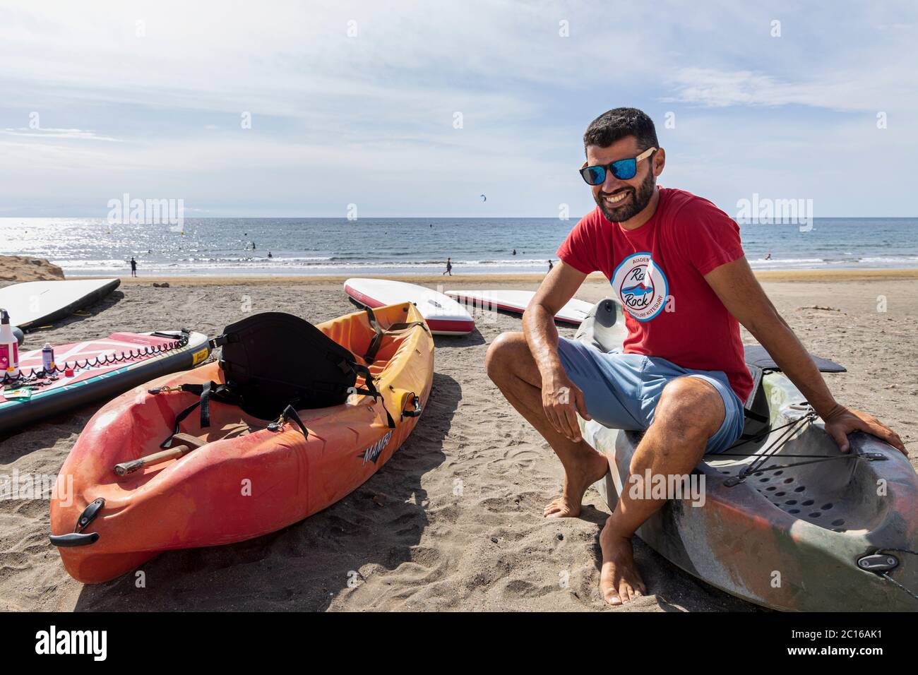 Local residents have the beach to themselves as the weather hots up for summer. Owner at Red Rock Surf prepares kayaks for hire. Phase 3 de-escalation Stock Photo