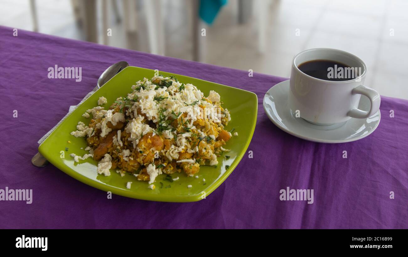 TIGRILLO is a typical dish consisting of ground green banana with cheese served in a green plate on a purple table accompanied with a cup of coffee wi Stock Photo