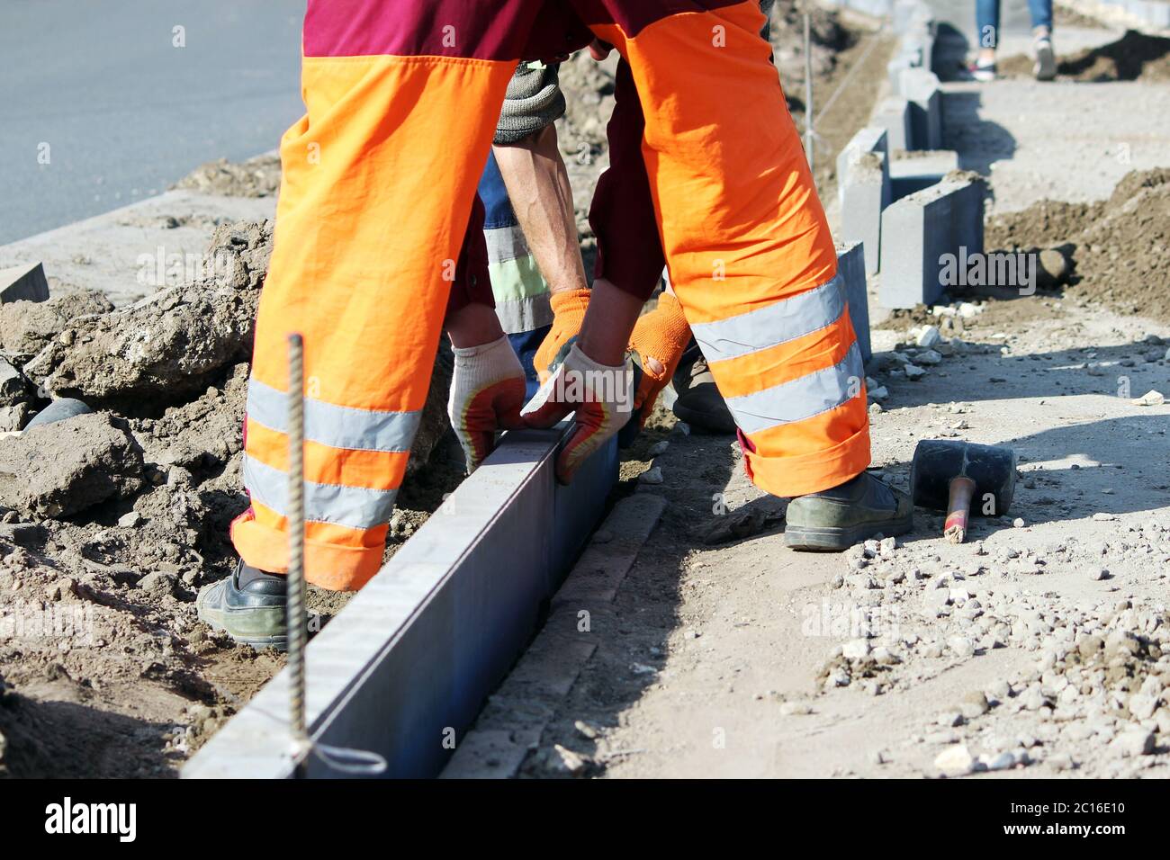 Repair of the sidewalk. Professional working masons in overalls lay curbs before laying stone paving slabs. Stock Photo