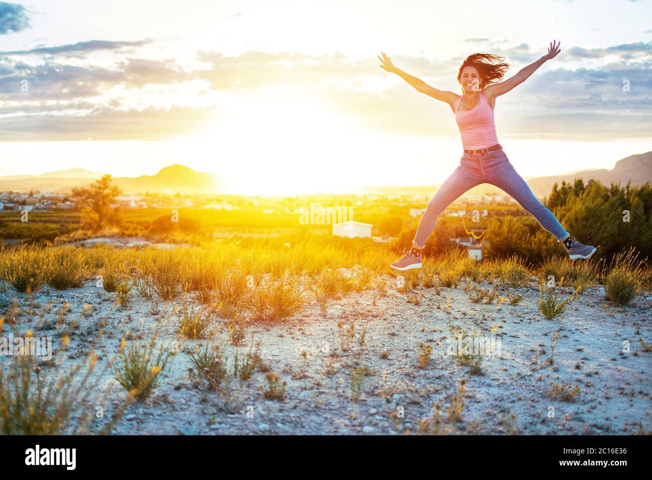 Athletic young girl jumping freely at mountain top against sunset