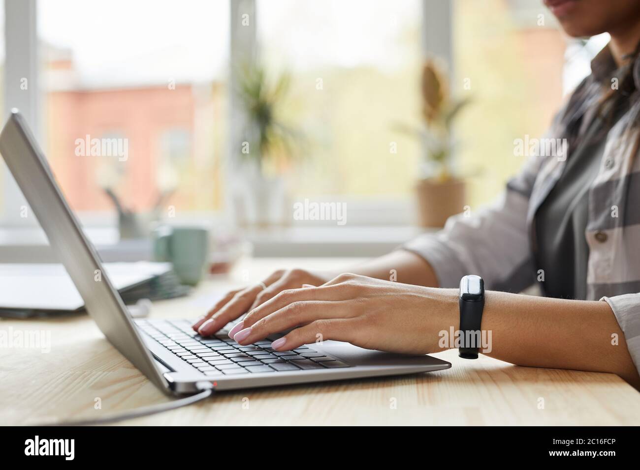 Side view close up of young mixed-race woman using laptop while working at home office, hands typing on keyboard, copy space Stock Photo
