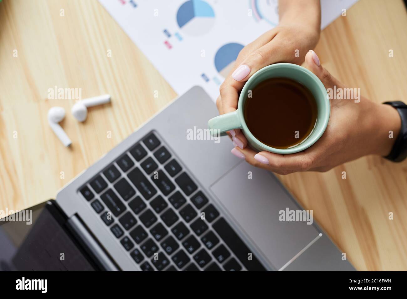 Above view at young woman holding coffee mug over laptop while working at home office, copy space Stock Photo