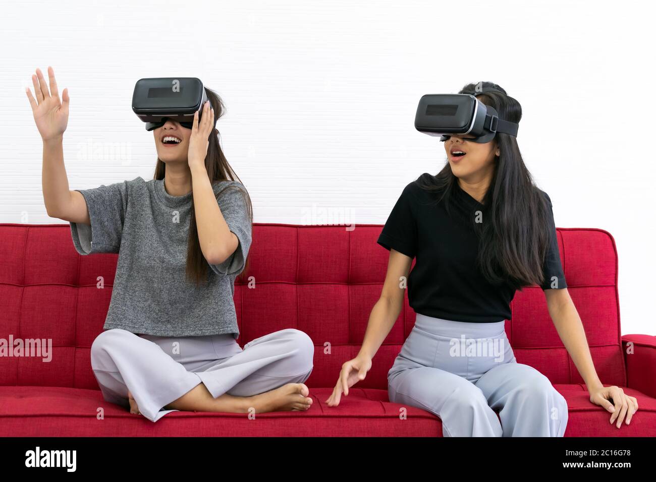Two Asian beautiful women smiling during playing VR video games experience in living room house for good mental health while quarantine. Game technolo Stock Photo