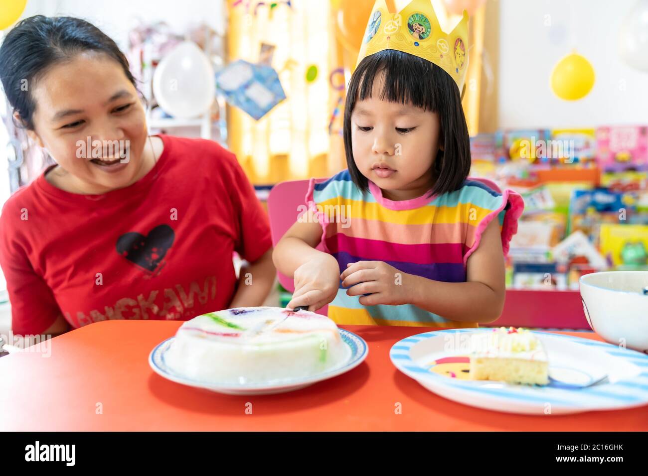 Asian girl kid cutting her birthday cake celebrate with mom alone because city lockdown while COVID-19 Pandemic. Celbration and quarantine concept. Stock Photo