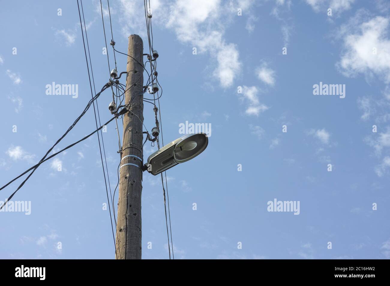An old electric wooden pole with a lamp and electricity cables hanging on. Natural light. Stock Photo