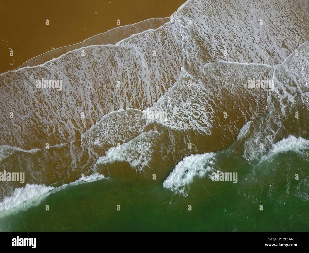 Aerial view of a wide sandy beach with large arriving and breaking