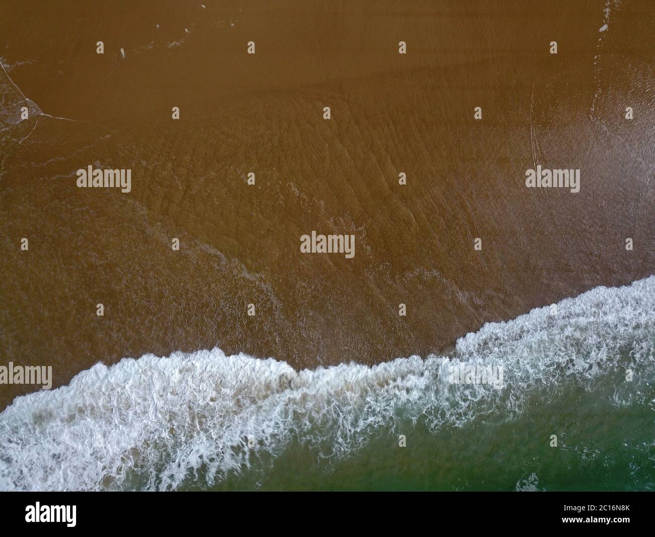 Aerial view of a wide sandy beach with large arriving and breaking