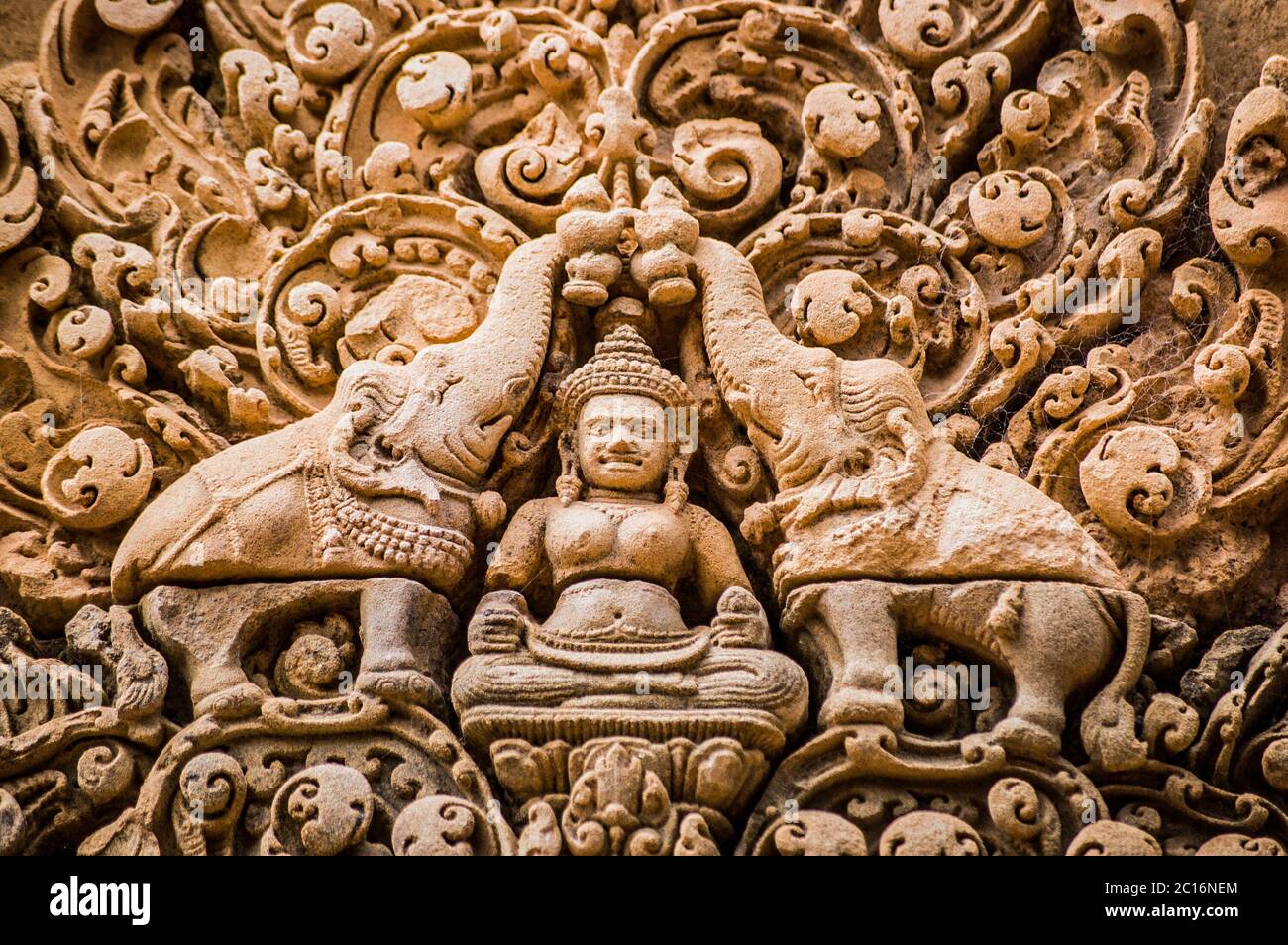 Ornate bas relief carving of the Hindu god Indra surrounded by elephants. Red sandstone lintel at the ancient Banteay Srei Temple, Angkor, Cambodia. Stock Photo