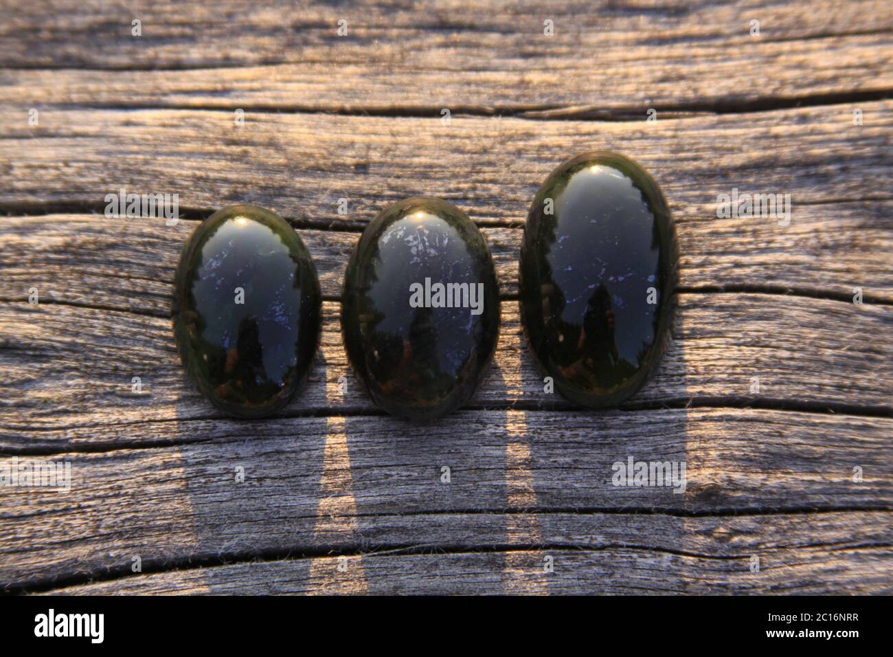 Black jade translucent green stone in sunlight on wood. The black jade